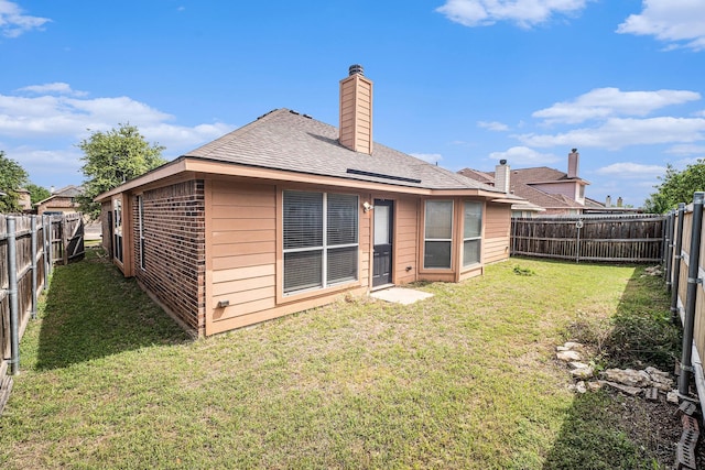 rear view of house featuring a fenced backyard, a chimney, and a lawn