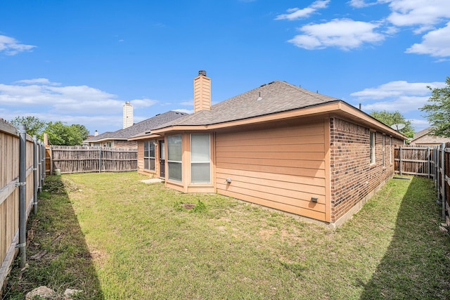 back of house featuring a lawn, a chimney, a fenced backyard, brick siding, and roof with shingles