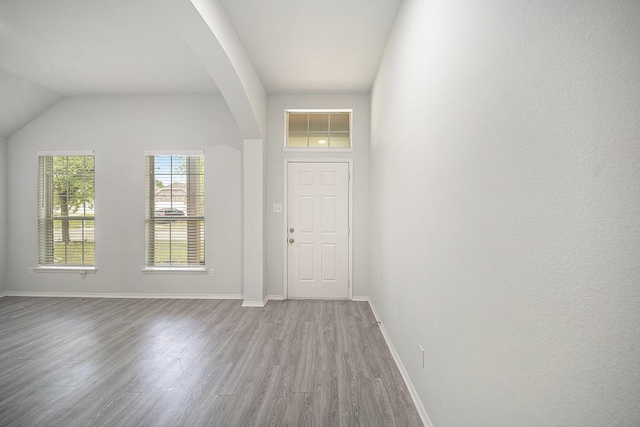 entryway with arched walkways, wood finished floors, and baseboards