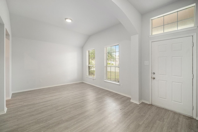 entrance foyer with arched walkways, wood finished floors, baseboards, and vaulted ceiling