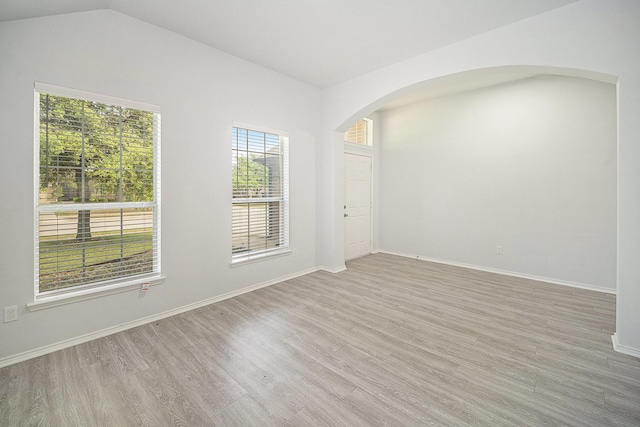 unfurnished room with arched walkways, light wood finished floors, baseboards, and lofted ceiling