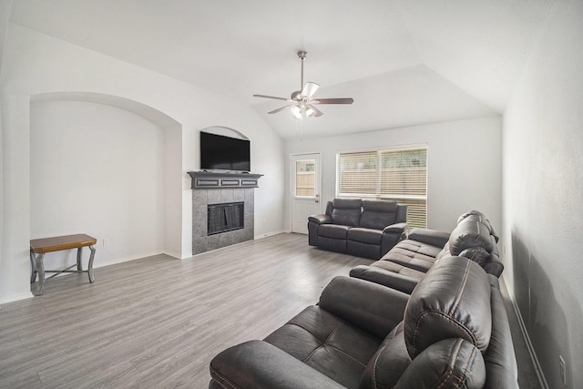 living area with wood finished floors, ceiling fan, lofted ceiling, and a tile fireplace