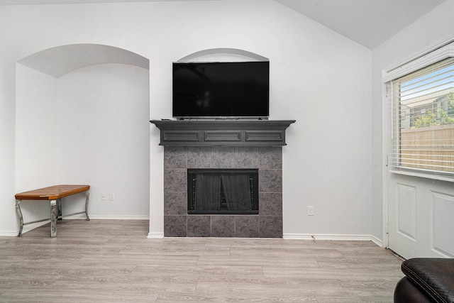 unfurnished living room featuring baseboards, wood finished floors, a tiled fireplace, and vaulted ceiling