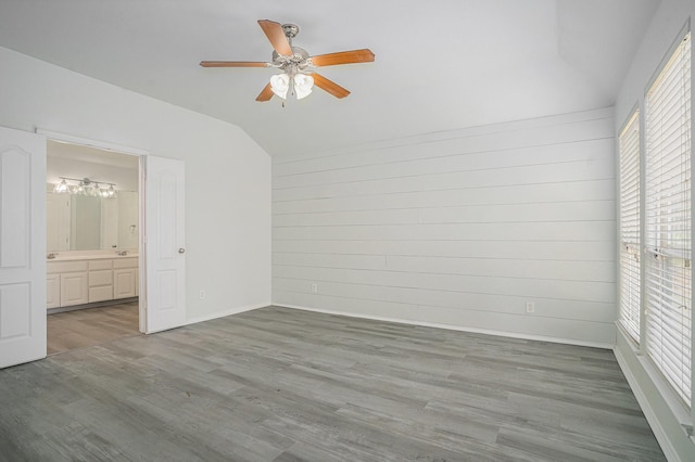 unfurnished bedroom with baseboards, connected bathroom, lofted ceiling, ceiling fan with notable chandelier, and wood finished floors
