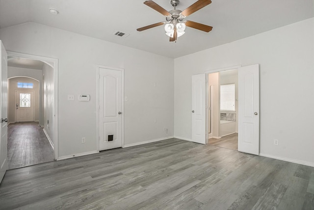 unfurnished bedroom featuring arched walkways, wood finished floors, baseboards, and visible vents