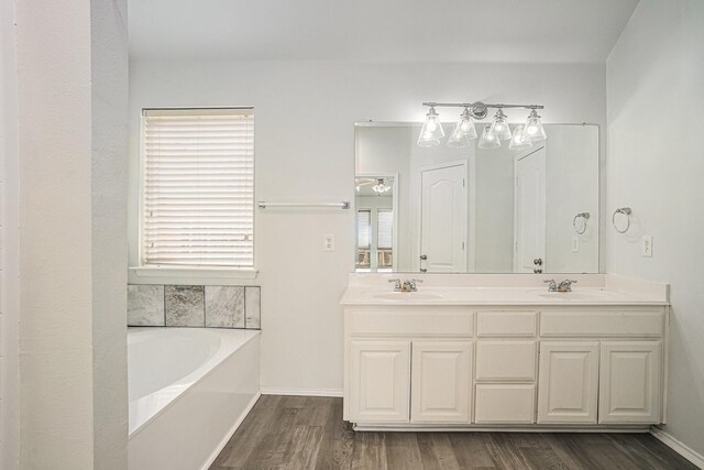 full bath featuring a bath, wood finished floors, double vanity, and a sink