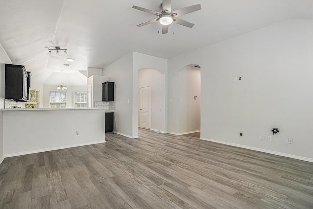 unfurnished living room featuring baseboards, vaulted ceiling, ceiling fan, arched walkways, and wood finished floors