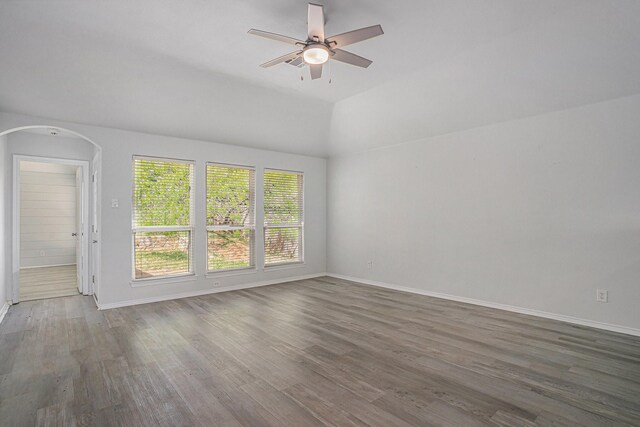 empty room with arched walkways, a ceiling fan, vaulted ceiling, wood finished floors, and baseboards