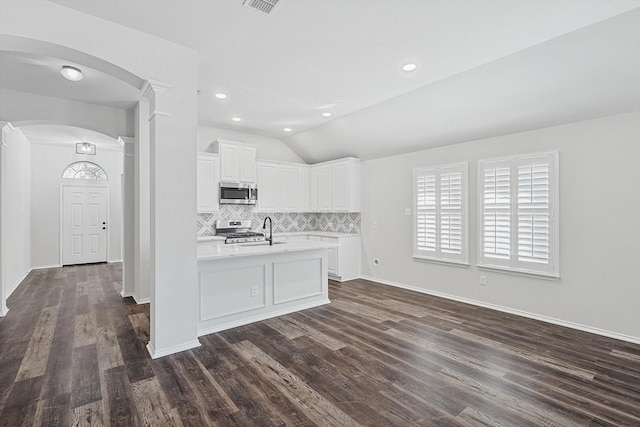 kitchen with dark wood-type flooring, appliances with stainless steel finishes, backsplash, white cabinets, and vaulted ceiling