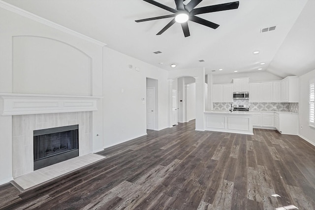 unfurnished living room featuring sink, vaulted ceiling, dark hardwood / wood-style floors, a tile fireplace, and ceiling fan