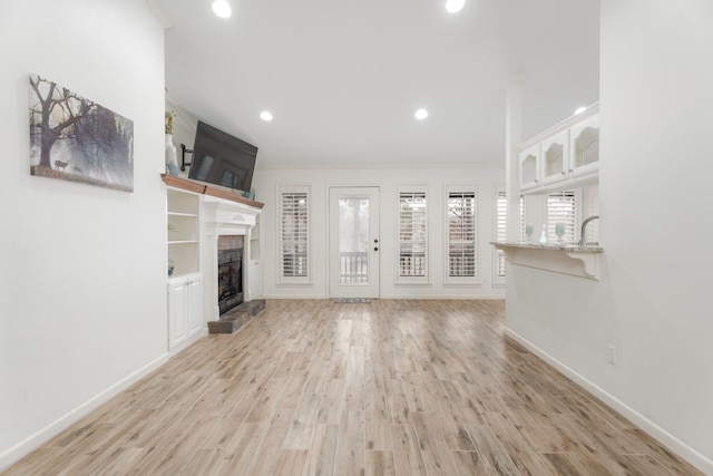 unfurnished living room featuring crown molding, a fireplace, and light hardwood / wood-style flooring