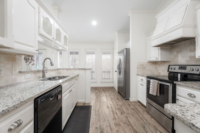 kitchen with premium range hood, white cabinetry, stainless steel appliances, light stone counters, and sink