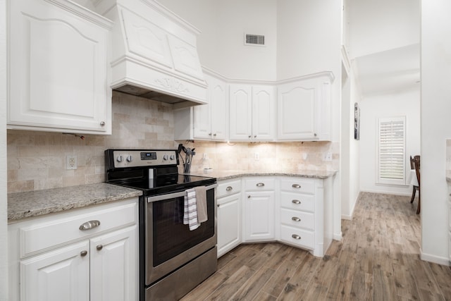 kitchen featuring light hardwood / wood-style floors, premium range hood, white cabinetry, and stainless steel electric range oven