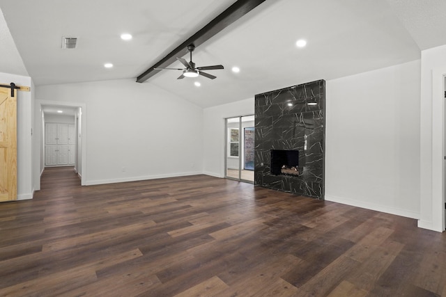 unfurnished living room featuring a premium fireplace, vaulted ceiling with beams, dark hardwood / wood-style floors, ceiling fan, and a barn door