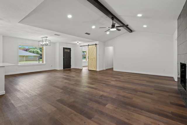 unfurnished living room featuring a barn door, ceiling fan, dark hardwood / wood-style flooring, a tile fireplace, and lofted ceiling with beams