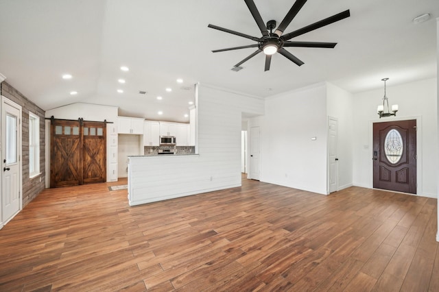 unfurnished living room featuring light wood-type flooring, ceiling fan with notable chandelier, and a barn door