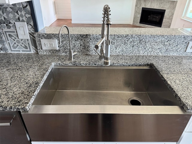 details with light stone countertops, sink, a tile fireplace, and tasteful backsplash