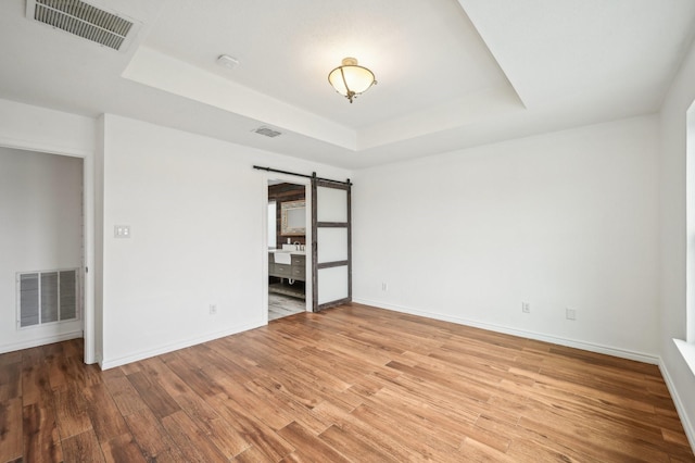 empty room with hardwood / wood-style floors, a barn door, and a raised ceiling