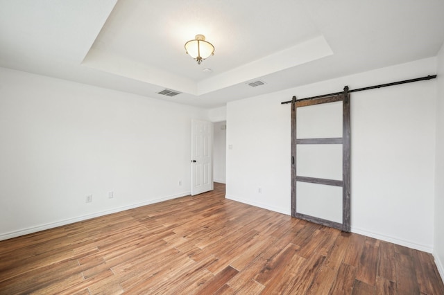 spare room with wood-type flooring, a barn door, and a raised ceiling