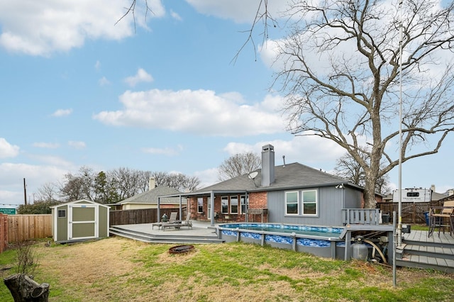 back of property featuring a swimming pool side deck, an outdoor fire pit, a storage shed, and a lawn