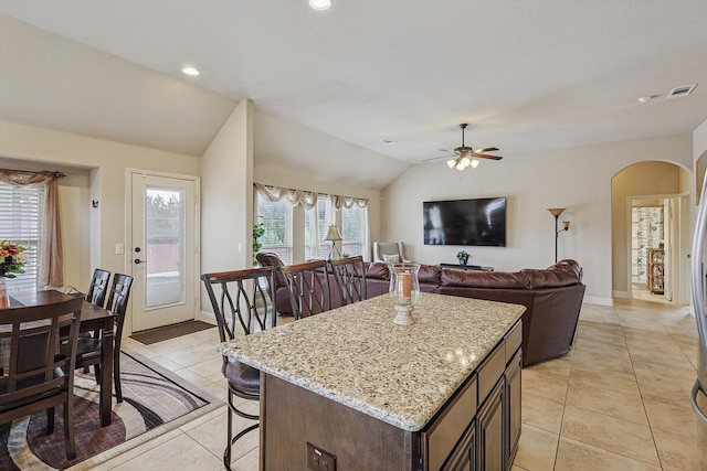 kitchen featuring a kitchen breakfast bar, vaulted ceiling, ceiling fan, light tile patterned flooring, and a kitchen island