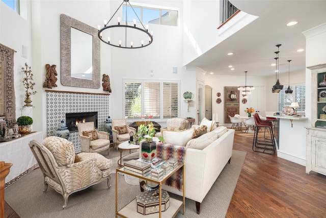 living room with an inviting chandelier, dark wood-type flooring, a fireplace, and a towering ceiling