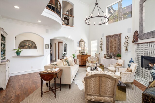 living room featuring a tile fireplace, hardwood / wood-style flooring, a high ceiling, crown molding, and an inviting chandelier