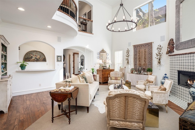 living room featuring a notable chandelier, a tile fireplace, crown molding, and wood finished floors