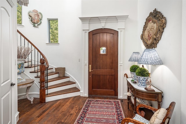 foyer entrance featuring stairs, dark wood-type flooring, and baseboards