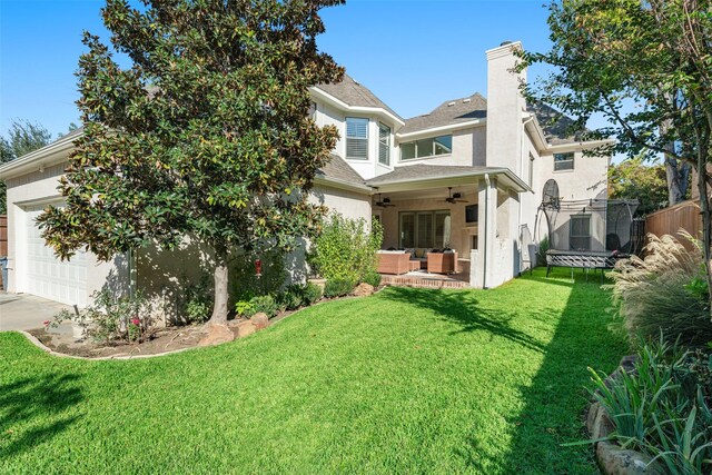 back of house featuring a garage, ceiling fan, a chimney, a trampoline, and a yard