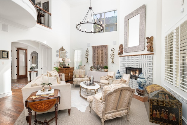 living area featuring wood finished floors, a tile fireplace, a towering ceiling, an inviting chandelier, and arched walkways