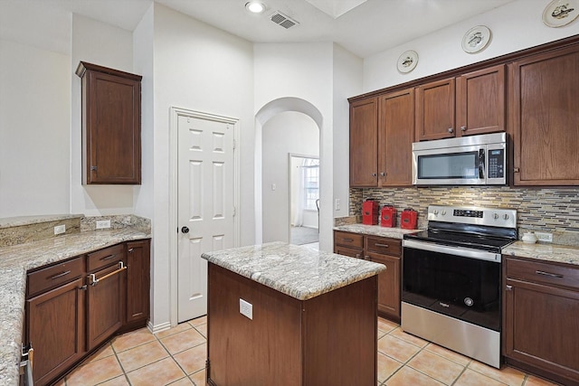 kitchen with light tile patterned floors, backsplash, light stone counters, and stainless steel appliances