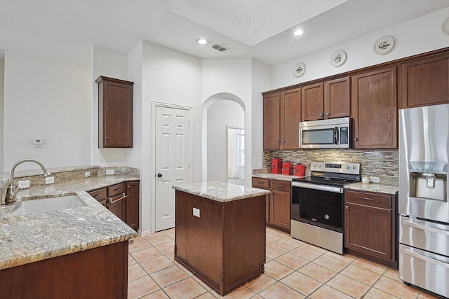 kitchen featuring light stone countertops, sink, stainless steel appliances, and a kitchen island