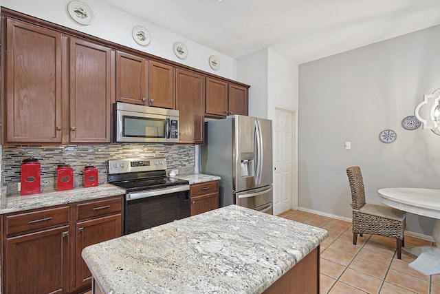 kitchen with decorative backsplash, appliances with stainless steel finishes, light stone counters, and a kitchen island