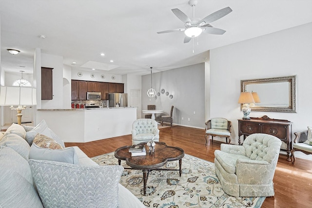 living room with ceiling fan with notable chandelier and light hardwood / wood-style floors