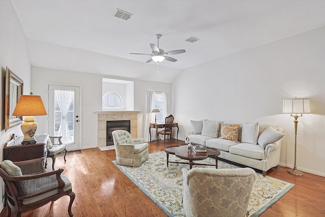 living room with ceiling fan, vaulted ceiling, a tile fireplace, and hardwood / wood-style floors