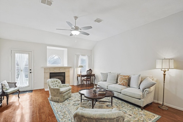 living room featuring vaulted ceiling, ceiling fan, a tiled fireplace, and wood-type flooring