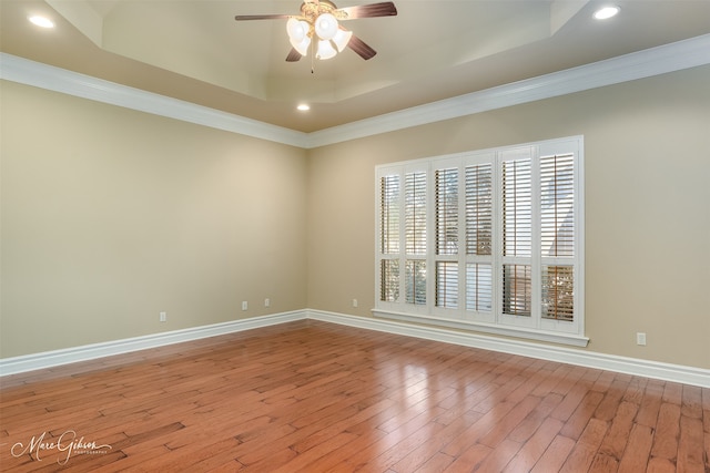 spare room with light wood-type flooring, ceiling fan, ornamental molding, and a tray ceiling