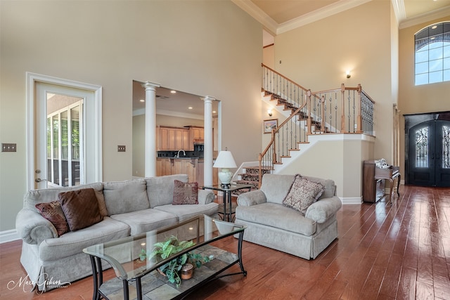 living room with a towering ceiling, sink, dark hardwood / wood-style floors, decorative columns, and crown molding