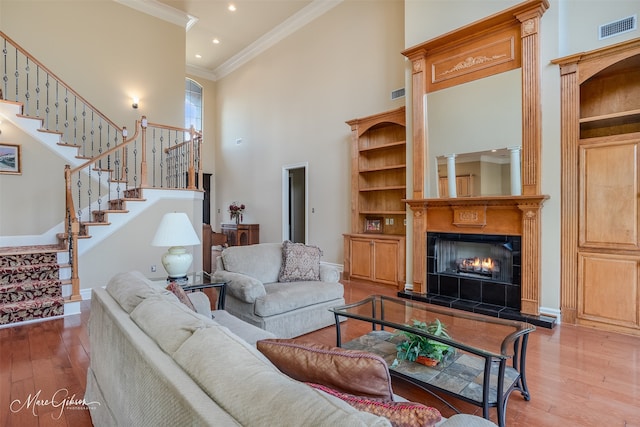 living room featuring a fireplace, a towering ceiling, ornamental molding, and hardwood / wood-style flooring