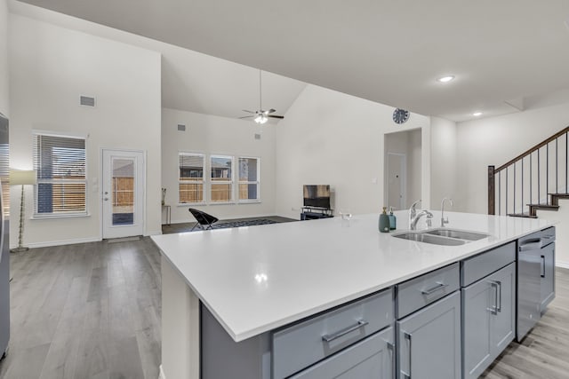 kitchen featuring vaulted ceiling, a center island with sink, stainless steel dishwasher, sink, and light wood-type flooring