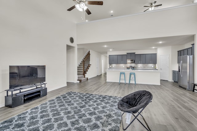 living room featuring ceiling fan, a high ceiling, and light hardwood / wood-style flooring