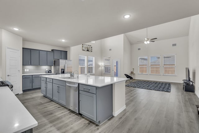 kitchen featuring light hardwood / wood-style floors, appliances with stainless steel finishes, gray cabinetry, tasteful backsplash, and a kitchen island with sink