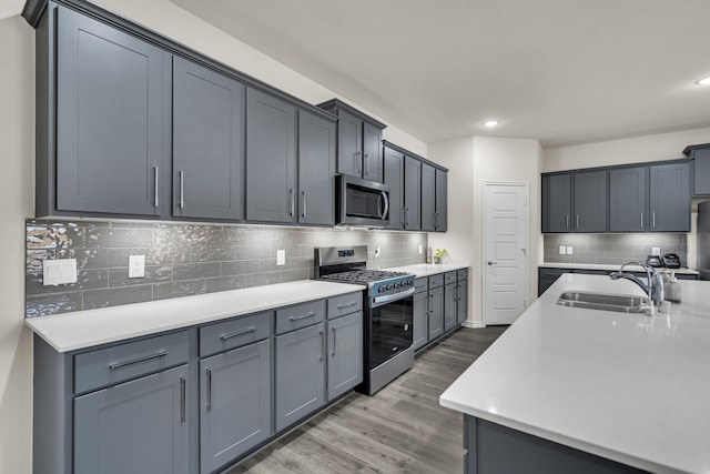 kitchen with wood-type flooring, stainless steel appliances, decorative backsplash, sink, and gray cabinetry