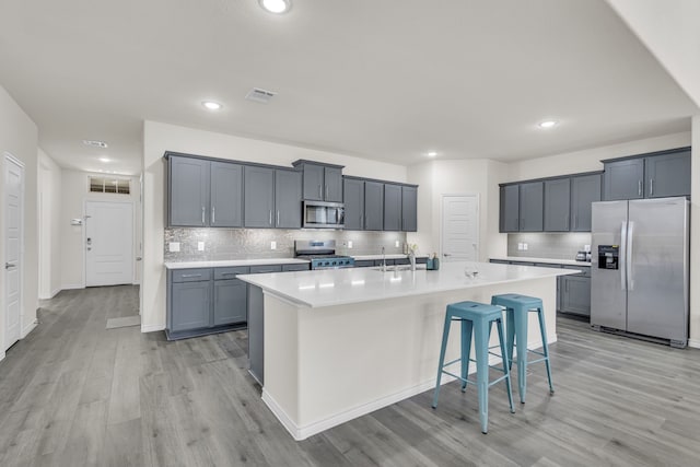 kitchen featuring gray cabinets, stainless steel appliances, a kitchen island with sink, a kitchen breakfast bar, and light wood-type flooring