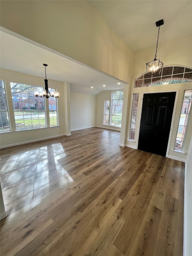 foyer entrance with vaulted ceiling, an inviting chandelier, and hardwood / wood-style flooring