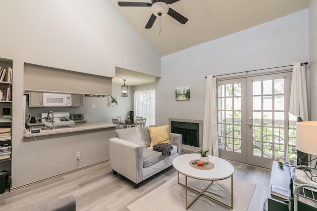 living room with ceiling fan, sink, light hardwood / wood-style flooring, high vaulted ceiling, and french doors