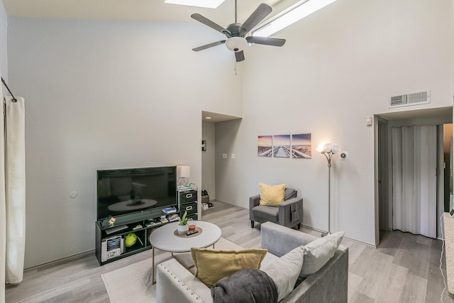 living room featuring high vaulted ceiling, light hardwood / wood-style floors, a skylight, and ceiling fan