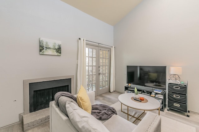 living room with a brick fireplace, light hardwood / wood-style flooring, high vaulted ceiling, and french doors