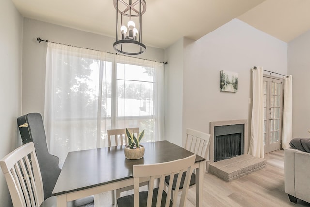 dining space with light wood-type flooring, a brick fireplace, and an inviting chandelier